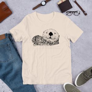 Soft cream Pen & Ink Sea Otter Head T-shirt laid flat with jeans, sneakers, a watch and glasses