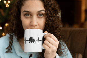 Curly-haired person sipping from the River Otter Heartbeat mug