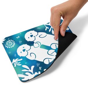A hand lifts the corner of the Sea Otter Tie Dye Mouse Pad, revealing its black underside and displaying a blue background with white cartoon sea otters and aquatic plant designs.