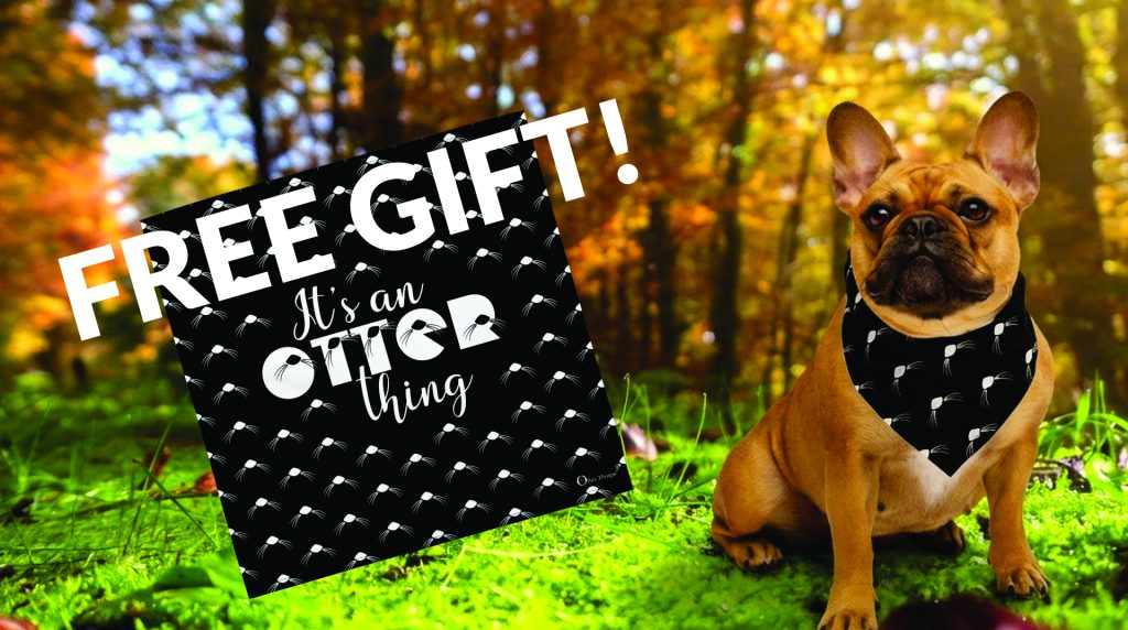 A brown French Bulldog wearing a black bandana with white otter prints sits on grass in a sunlit forest. Next to the dog is a sign reading "FREE GIFT! It’s an otter thing" with the same otter print background.