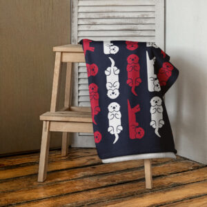 A Sea Otter USA Flag Beach Towel, featuring playful sea otters and flag motifs, is draped over a wooden chair on a rustic wooden floor beside white shuttered doors.
