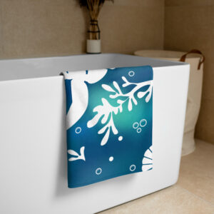 A white bathtub features the Sea-Otter-Tie-Dye-Beach-Towel, blue and white patterned, draped over its side. In the background, a vase of dried plants sits on the tub ledge next to a laundry basket with a leather handle.