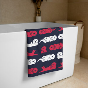 The Sea Otter USA Flag Beach Towel, featuring red, white, and blue otter designs, hangs over a modern white bathtub in a beige-tiled bathroom. A vase with dried plants and a laundry basket can be seen in the background.