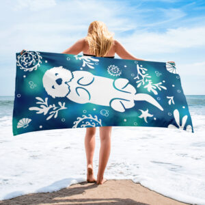 Person on a sandy beach holding up the Sea Otter Tie-Dye beach towel toward the ocean