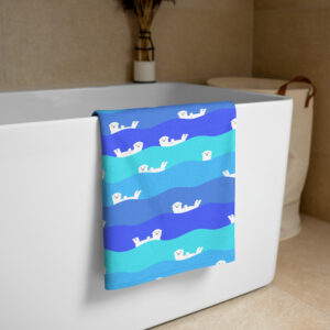 The Ocean Otter Gradient Beach Towel with playful otter illustrations hangs over a white bathtub in a beige-tiled bathroom, with a basket and dried plant vase in the background.