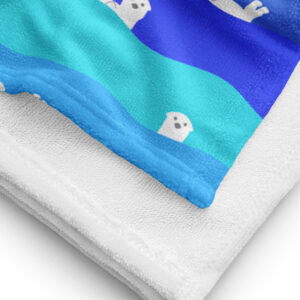 A close-up of the Ocean Otter Gradient Beach Towel shows its white underside and a vibrant top with blue waves and playful white cartoon otter faces.
